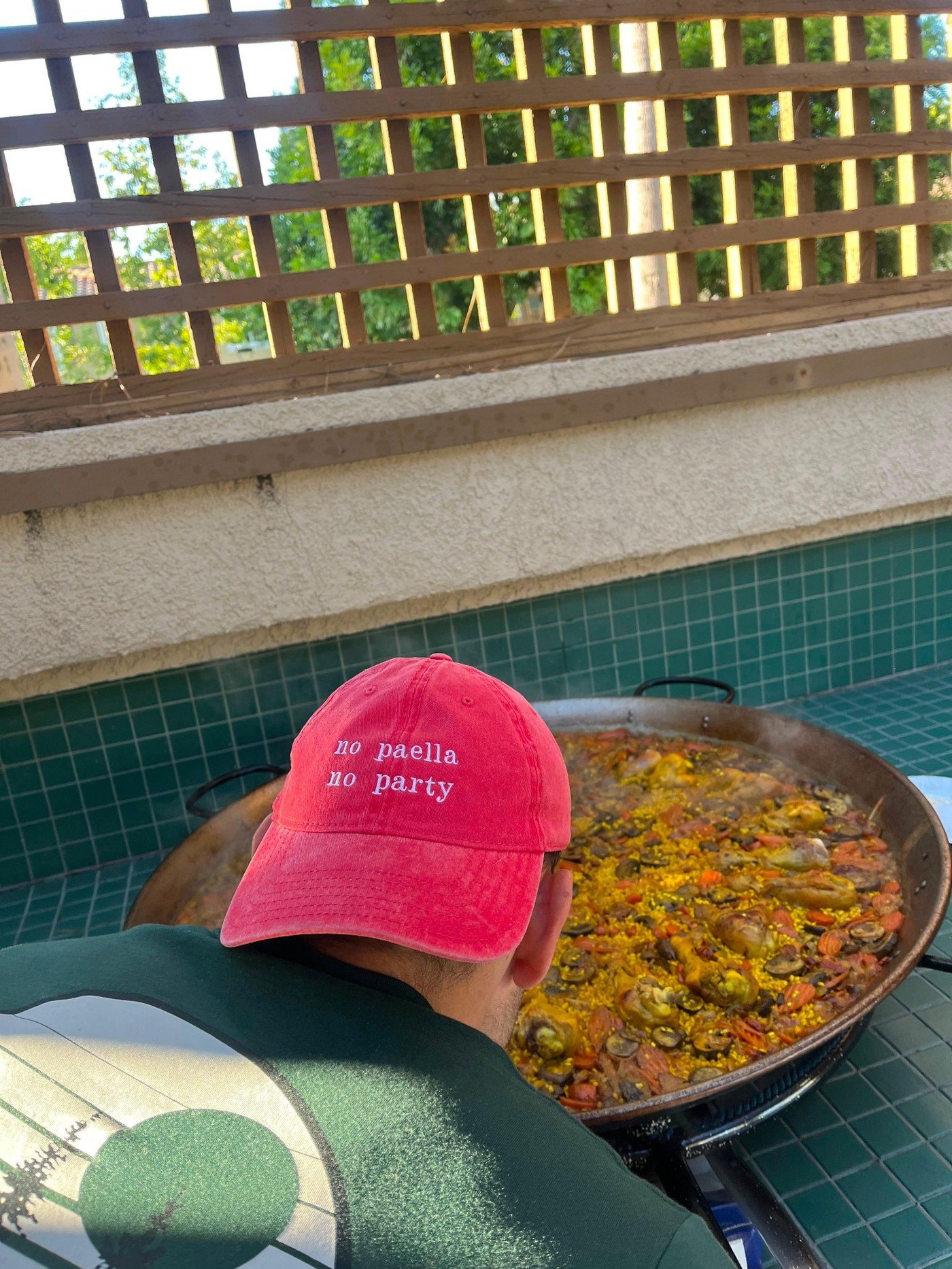 Pau cooking paella wearing a red cap that says no paella no party